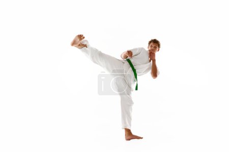 Téléchargez les photos : Athlète sportif de combat, jeune homme en kimono blanc, pratiquant le karaté isolé sur fond de studio blanc. Concept d'arts martiaux, sport de combat, énergie, force, santé. Publicité - en image libre de droit