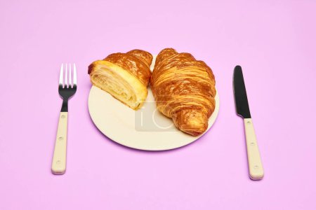 Foto de Croissant crujiente, fresco, entero y cortado por la mitad acostado en el plato sobre fondo rosa. Concepto de comida, panadería, ideas de desayuno, sabor, frescura. Poser. Copiar espacio para anuncio - Imagen libre de derechos