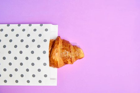 Photo for Piece of crispy, freshly baked croissant peaking out paper packaging isolated over pink background. Concept of food, bakery, breakfast ideas, taste, freshness. Poser. Copy space for ad - Royalty Free Image