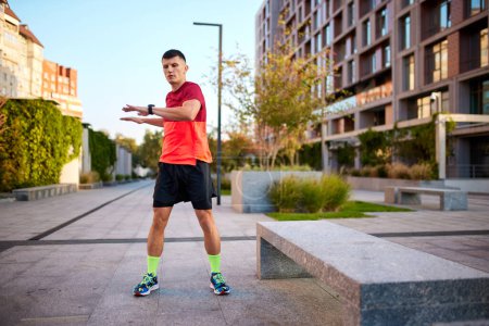 Photo for Warming-up muscles before training. Man in sportswear standing on empty street and doing exercises. Concept of sport, active and healthy lifestyle, competition, dynamics, marathon - Royalty Free Image