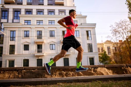 Photo for Dynamic image of man, professional runner in motion, training, running along empty street on warm morning. Concept of sport, active and healthy lifestyle, competition, dynamics, marathon - Royalty Free Image