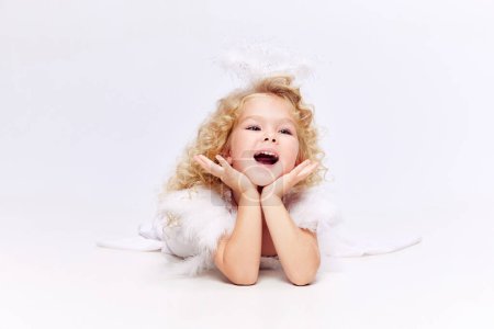 Foto de Niño feliz, sonriente, linda niña en vestido blanco en imagen de ángel de pie aislado sobre fondo de estudio blanco. Concepto de infancia, imaginación, fantasía, moda y belleza, vacaciones - Imagen libre de derechos