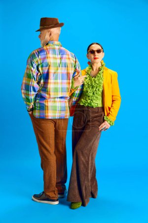 Photo for Support and love. Elegant, stylish couple, senior man and woman in fashionable clothes standing against blue studio background. Concept of beauty and fashion, relationship, modern style, age - Royalty Free Image
