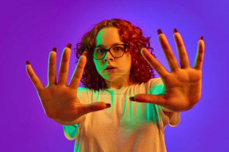 Photo for Teen girl emotional spreading hands with terrified face against purple background in neon light. Concept of human emotions, lifestyle, youth, facial expression. Ad - Royalty Free Image