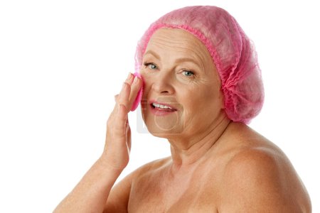 Foto de Senior hermosa mujer lavándose la cara, usando cepillo de goma para una limpieza profunda sobre fondo blanco del estudio. Concepto de belleza natural, proceso de envejecimiento, belleza anciana, cosmetología, cuidado de la piel - Imagen libre de derechos