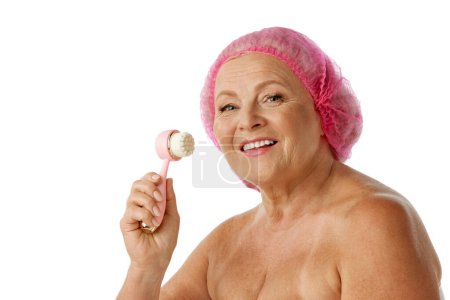 Photo for Senior beautiful woman cleaning her face, using special brush for deep cleansing against white studio background. Concept of natural beauty, aging process, elderly beauty, cosmetology, skincare - Royalty Free Image