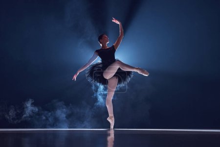 Foto de Mujer joven elegante y talentosa, bailarina profesional en movimiento, bailando sobre fondo oscuro con efecto de humo. Concepto de danza clásica, arte y gracia, belleza, coreografía, inspiración - Imagen libre de derechos