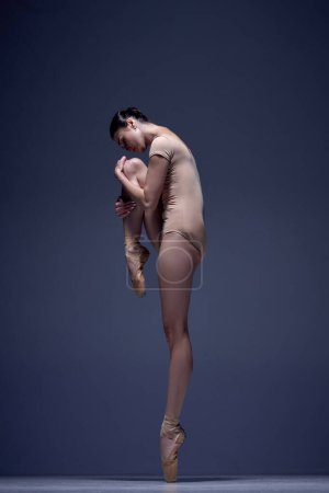 Photo for Elegant, attractive woman, professional ballerina in beige bodysuit, standing in pointe against blue studio background. Concept of classical dance, art and grace, beauty, choreography, inspiration - Royalty Free Image