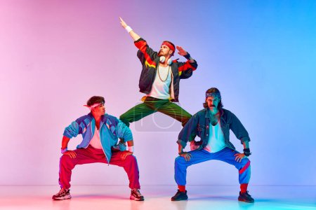 Photo for Team. Friends, tree men in colorful retro sportswear standing in pyramid pose against gradient pink blue background in neon light. Concept of sportive and active lifestyle, humor, retro style. Ad - Royalty Free Image