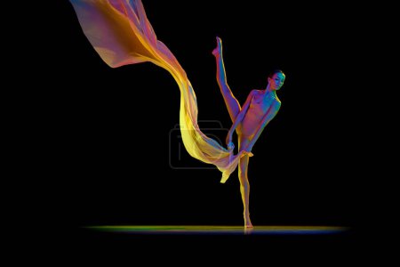 Foto de Mujer joven elegante flexible, bailarina en traje de cuerpo beige bailando con tela transparente aislada sobre fondo negro en luz de neón. Concepto de belleza, danza clásica, arte, elegancia, coreografía - Imagen libre de derechos