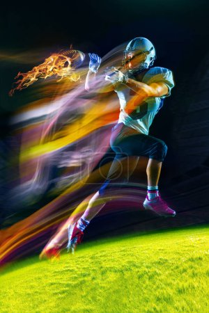 Foto de Jugador de fútbol americano en movimiento durante el juego, corriendo con pelota sobre fondo oscuro en luz mixta de neón. Bola ardiente. Concepto de evento deportivo, campeonato, apuestas, juego. Póster para anuncio - Imagen libre de derechos