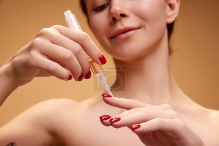 Photo for Focus on hands. Young pretty girl taking care after hands, applying cuticle oil isolated over light brown background. Concept of natural beauty, skincare, cosmetics and cosmetology - Royalty Free Image