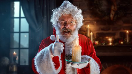 Photo for Senior bearded man in classes, Santa Claus standing in room with candles in the evening. Decorated room on background. Concept of winter season, holidays, fantasy, joy and fun, Christmas - Royalty Free Image