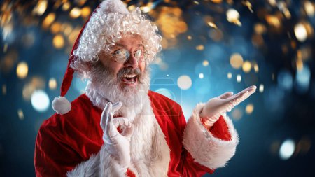 Photo for Time for miracles and fantasy. Senior bearded man, Santa Claus standing over dark blue background with light. Celebration. Concept of winter season, holidays, fantasy, joy and fun, Christmas - Royalty Free Image