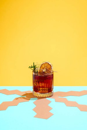 Photo for Glass with fresh, delicious Negroni cocktail decorated with slice of dry orange and rosemary over yellow background. Concept of alcohol drinks, party, holidays, bar, mix. Poster. Copy space for ad - Royalty Free Image