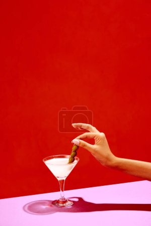 Photo for Traditional original drink. Glass with martini decorated with olives isolated over red background. Salty taste of appetizer. Concept of alcohol drinks, party, holidays, bar. Poster. Copy space for ad - Royalty Free Image