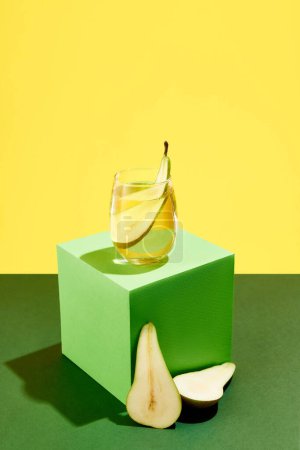 Téléchargez les photos : Délicieux cocktail sucré au goût de poire debout sur un cube vert sur fond jaune. Goût d'été. Concept de boissons alcoolisées, fête, vacances, bar, mix. Affiche. Espace de copie pour la publicité - en image libre de droit