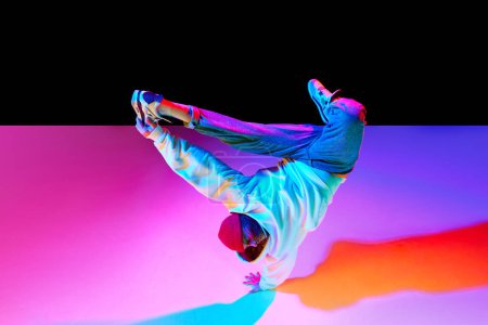 Foto de Atlético joven en movimiento, bailando breakdance aislado sobre fondo de estudio negro en luz de neón. Concepto de danza contemporánea, estilo callejero, moda, hobby, juventud. Anuncio - Imagen libre de derechos