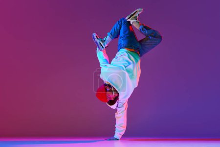 Photo for Man in stylish sportswear in motion, dancing breakdance isolated over gradient studio background in neon light. Concept of contemporary dance, street style, fashion, hobby, youth. Ad - Royalty Free Image