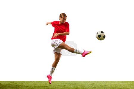 Foto de Imagen dinámica de la joven, jugador de fútbol en movimiento durante el juego, golpeando la pelota en un salto aislado sobre fondo blanco. Concepto de deporte, competición, acción, éxito, motivación. Copiar espacio para anuncio - Imagen libre de derechos