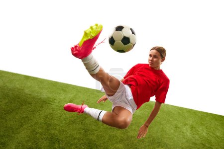 Foto de Jugadora de fútbol femenina concentrada en movimiento, golpeando la pelota y cayendo durante el juego en el campo de hierba aislada sobre fondo blanco. Concepto de deporte, competición, acción, éxito. Copiar espacio para anuncio - Imagen libre de derechos