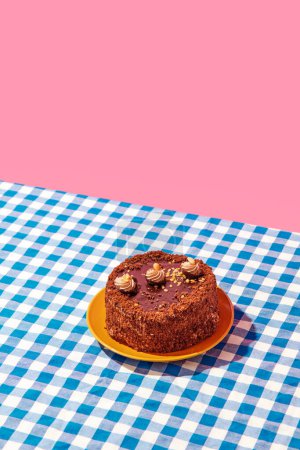 Téléchargez les photos : Gâteau délicieux au chocolat sur plaque sur nappe à carreaux bleus sur fond rose. Concept de nourriture, desserts, fête d'anniversaire, fête, boulangerie. Style pop art. Espace de copie pour l'annonce. Affiche - en image libre de droit