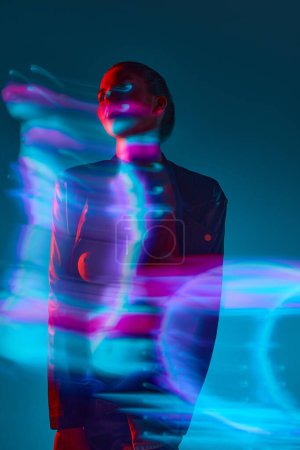 Foto de Silueta de mujer joven de pie sobre fondo azul con efecto de luces de neón mixtas. Holograma. Concepto de arte moderno, belleza, estilo, futurismo y cyberpunk, creatividad - Imagen libre de derechos
