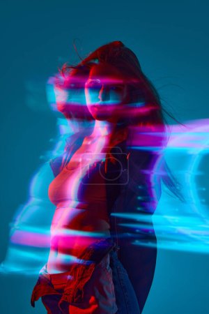 Foto de Silueta de mujer joven de pie sobre fondo azul con efecto de luces de neón mixtas. Holograma. Concepto de arte moderno, belleza, estilo, futurismo y cyberpunk, creatividad - Imagen libre de derechos