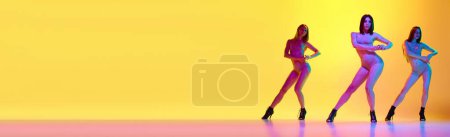 Téléchargez les photos : Image pleine longueur de trois jeunes femmes aux formes corporelles parfaites dansant sur des chaussures à talons sur fond jaune dégradé sous la lumière du néon. Concept de passe-temps, style de danse contemporaine, art, beauté, élégance - en image libre de droit