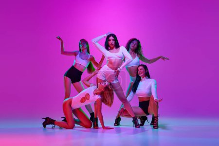Téléchargez les photos : Belles, élégantes, jolies femmes dansant talon haut danse sur fond studio rose dans la lumière au néon. Concept de passe-temps, style de danse contemporaine, art, beauté, créativité, élégance - en image libre de droit