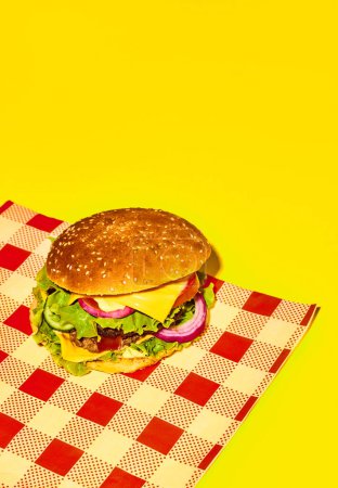 Photo for Delicious homemade burger, hamburger with fresh bun, meat, cheese, lettuce and tomato on checkered napkin on yellow background. Concept of fast food, taste, junk food. Complementary colors. Poster, ad - Royalty Free Image