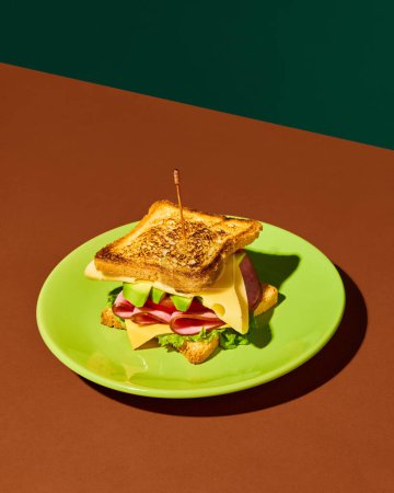 Foto de Placa con delicioso sándwich de club con jamón, lechuga, queso, tomate y aguacate sobre fondo verde rojo. Concepto de comida rápida, sabor, cocina, ingredientes. Colores complementarios. Póster, anuncio - Imagen libre de derechos