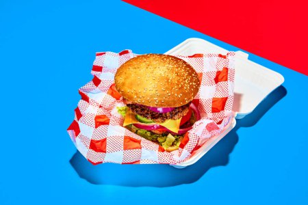 Photo for To go food. Delicious burger, hamburger with fresh bun meat, cheese, lettuce and tomato. Concept of fast food, taste, junk food. Complementary colors. Poster, ad - Royalty Free Image
