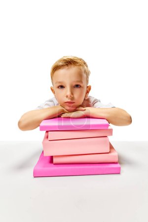 Photo for Cute little boy sitting at desk put his hands and head on stack of books. Child study and learn for preschool. Online education. Concept of childhood, International Knowledge Day, academic. ad - Royalty Free Image