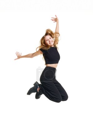 Young attractive girl, teenager with blonde hair jumping raising hands of joy and happiness isolated white background. Concept of beauty, youth, human emotions, fashion, style, modelling, sales, shop.