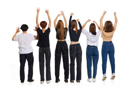 Foto de Vista trasera. Grupo de mujeres jóvenes y atractivas de pie levantando sus manos sobre fondo de estudio blanco. Copiar espacio. Concepto de belleza, juventud, emociones, moda, estilo, modelaje, estilo de vida. - Imagen libre de derechos