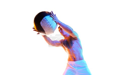 Téléchargez les photos : Jeune homme athlétique, sans chemise, fort, en forme, entraînement du corps de secours avec balle de remise en forme sur fond de studio blanc dans la lumière du néon. Concept de sport, mode de vie actif et sain, soins du corps, fitness - en image libre de droit