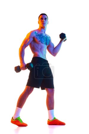 Photo for Full-length of shirtless young man with strong, muscular fit body training with dumbbells against white studio background in neon light. Concept of sport, active and healthy lifestyle, body, fitness - Royalty Free Image