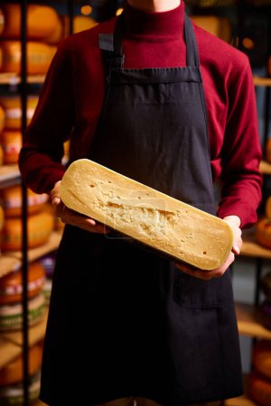 Foto de Hombre sosteniendo brocas de queso en lugares especiales para el almacenamiento y producción de queso. Comida ecológica. Queso añejo. Concepto de comida, gusto, arte de los productos orgánicos, comida sana, natural. - Imagen libre de derechos