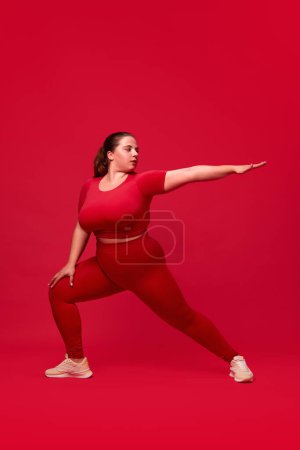 Photo for Plus size model. Young woman with fat, overweigh body training, doing exercises against red studio background. Concept of sport, body-positivity, weight loss, body, health care. - Royalty Free Image