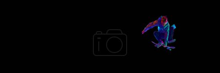 Photo for Sportive, active young man in casual clothes in motion, training with skateboard, doing stunts against black background in neon light. Concept of professional sport, competition, training, action - Royalty Free Image