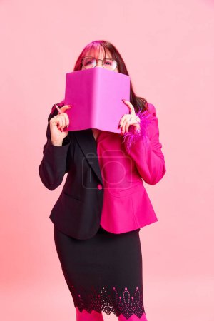 Photo for Young girl with pink hair, extraordinary clothes standing with notebook and smiling against pink studio background. Concept of youth, self-expression, fashion, emotions, business, employment - Royalty Free Image