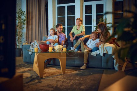 Photo for Beautiful young family, father, mother and children watching tv at home. People sitting on couch in living rooms. Parents discussing. Concept of family, leisure time, relaxation, childhood, parenthood - Royalty Free Image