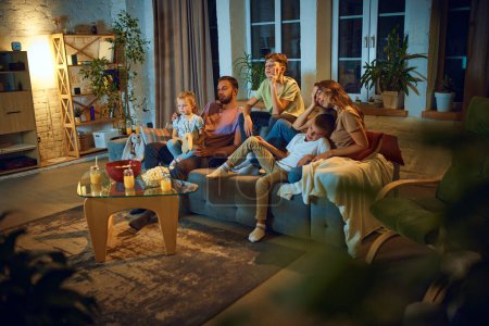 Photo for Family, mother, father and little kids, children sitting on couch at home and watching TV show. Feeling bored. Concept of family, leisure time, relaxation, childhood and parenthood - Royalty Free Image