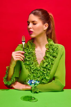 Photo for Portrait of attractive lady holds impaled on fork vitamin, tablet, pill and want to eat it and full of medication glass isolated red background. Concept of medicine, viruses, immune system, healthcare - Royalty Free Image