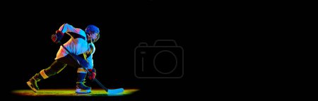 Photo for Young girl in uniform, hockey player standing with stick against black studio background in neon light. Concept of professional sport, competition, game, action, hobby. Empty space to insert your text - Royalty Free Image