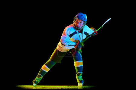 Photo for Competitive young girl, hockey player in motion during game, playing against black studio background in neon light. Champion. Concept of professional sport, competition, game, action, hobby - Royalty Free Image