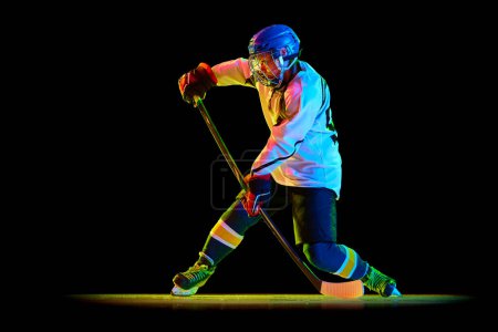 Foto de Mujer joven, jugador de hockey profesional en movimiento, entrenamiento, jugando contra fondo de estudio negro en luz de neón. Éxito. Concepto de deporte profesional, competición, juego, acción, hobby - Imagen libre de derechos