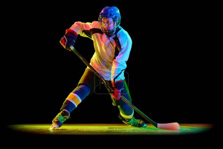 Photo for Young woman, professional hockey player in motion, training, playing against black studio background in neon light. Success. Concept of professional sport, competition, game, action, hobby - Royalty Free Image
