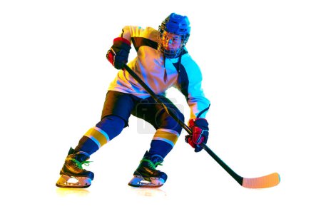 Foto de Chica joven, jugador de hockey en uniforme y entrenamiento de casco, de pie con palo sobre fondo blanco en luz de neón. Concepto de deporte profesional, competición, juego, acción, hobby, logro - Imagen libre de derechos